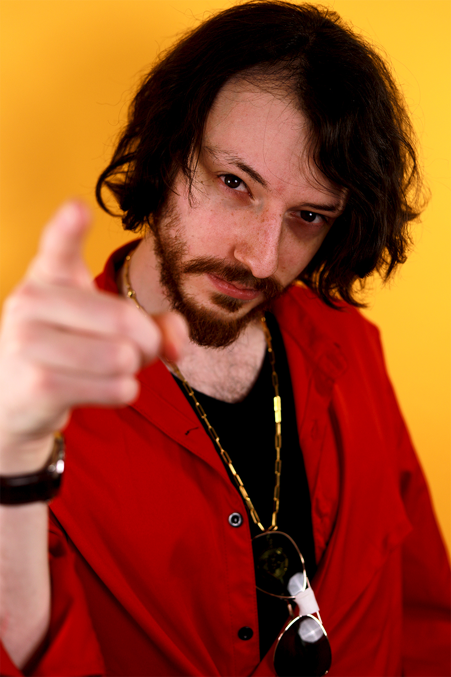 Torso shot of Rito pointing his finger up at the viewer in a yellow background wearing a red shirt