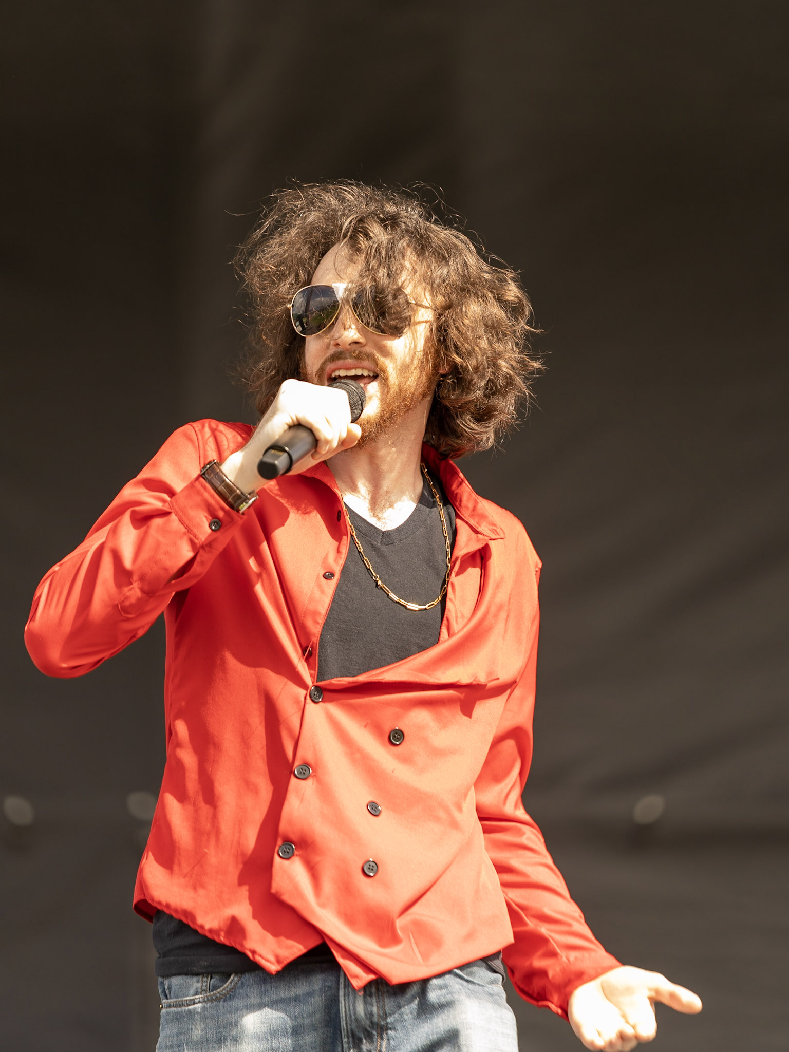 Rito holding a microphone to his mouth performing on stage wearing a red shirt